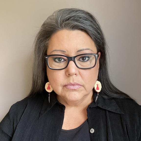 an Indigenous woman with black hair and glasses in a black shirt and black t-shirt