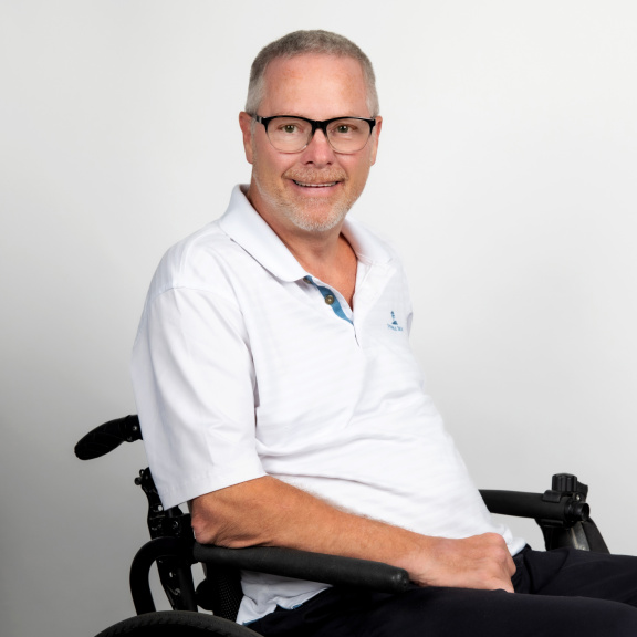 Caucasian male with glasses smiling in white t-shirt and in a wheelchair