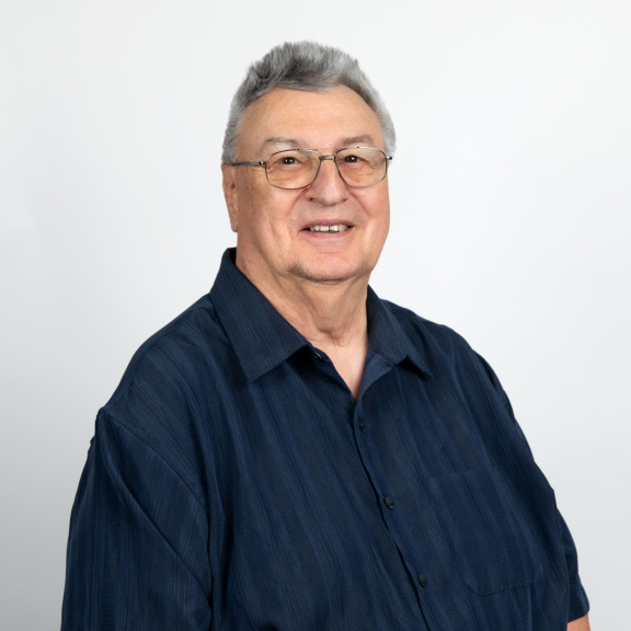 Smiling White man with short gray hair and glasses wearing a navy shirt.