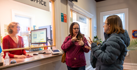 Two people at a service counter speaking in sign language, and a third is behind the counter
